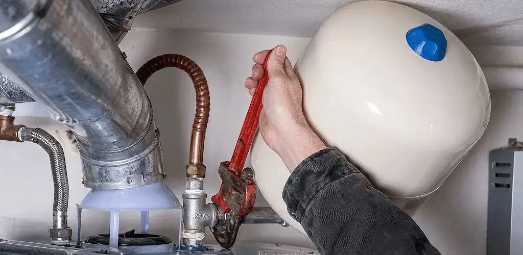 Water heater repair technician tightening plumbing connections near a tank unit in Kansas City, MO